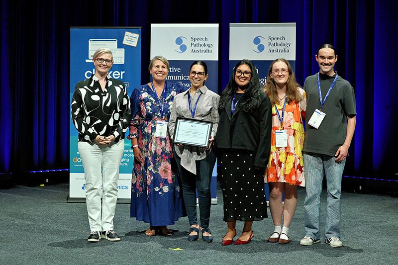 This is a photo of Dr Laura Chahda holding an JCPSLP Editor’s Award plaque as she poses with fellow winners Druvni Perera, Laura Knauer and Darcy Long. Emma Power and Dr Katrina Blyth stand to the left of them at the SPA 2026 Conference.